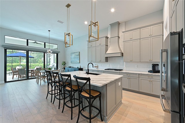 kitchen with decorative light fixtures, custom exhaust hood, a kitchen island with sink, and sink