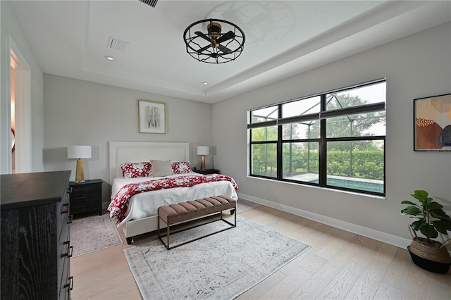 bedroom with light hardwood / wood-style floors and a raised ceiling