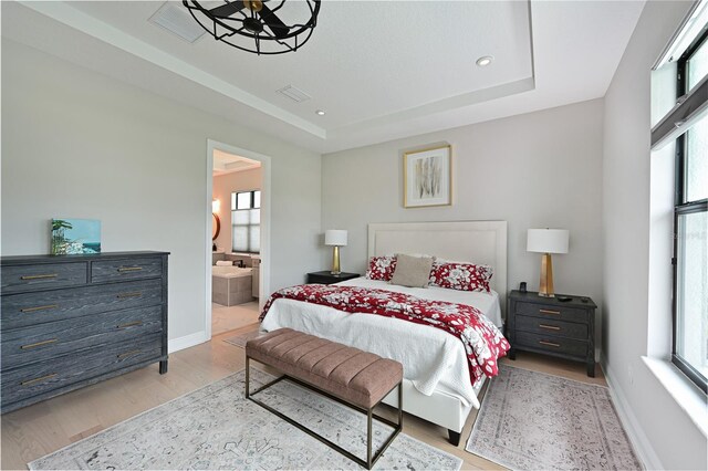 bedroom with a raised ceiling, ensuite bathroom, and light hardwood / wood-style floors