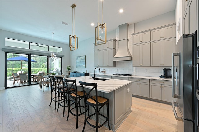 kitchen with gray cabinets, freestanding refrigerator, a sink, gas cooktop, and premium range hood