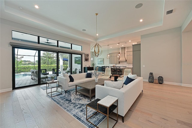 living area featuring baseboards, visible vents, an inviting chandelier, light wood-style flooring, and a raised ceiling