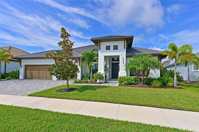 view of front of house with stucco siding, a front lawn, a tile roof, decorative driveway, and an attached garage