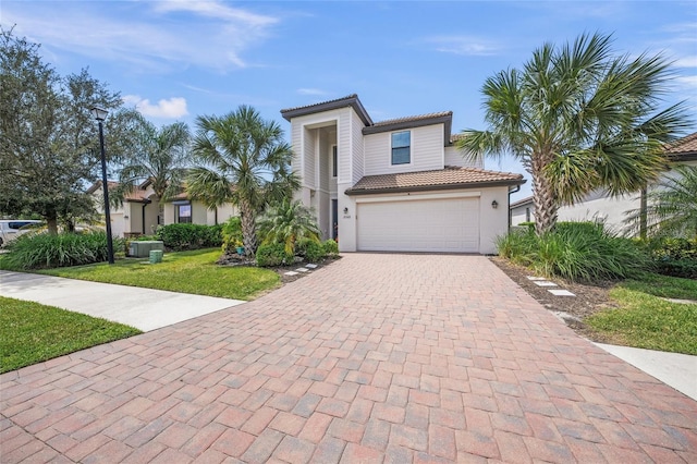 view of front facade featuring a garage, central AC unit, a tile roof, decorative driveway, and a front yard