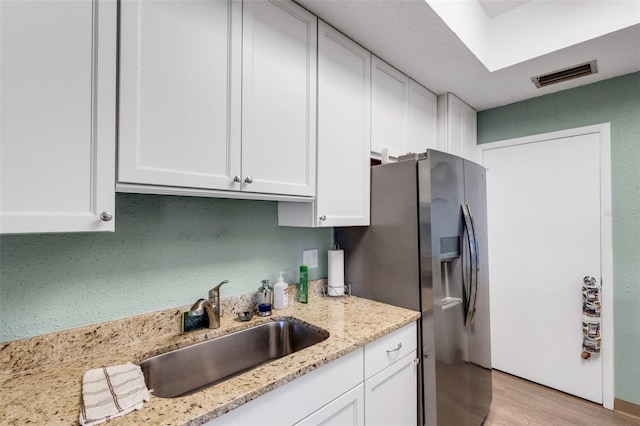 kitchen featuring sink, light stone countertops, white cabinetry, and light hardwood / wood-style floors