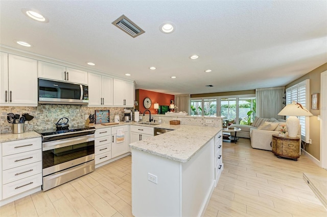 136 Crescent Dr, Anna Maria, FL 34216 - kitchen with visible vents, a sink, a peninsula, light wood finished floors, and stainless steel appliances