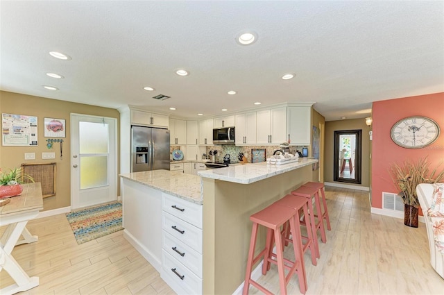 136 Crescent Dr, Anna Maria, FL 34216 - kitchen with a breakfast bar area, appliances with stainless steel finishes, light wood-type flooring, light stone counters, and a peninsula