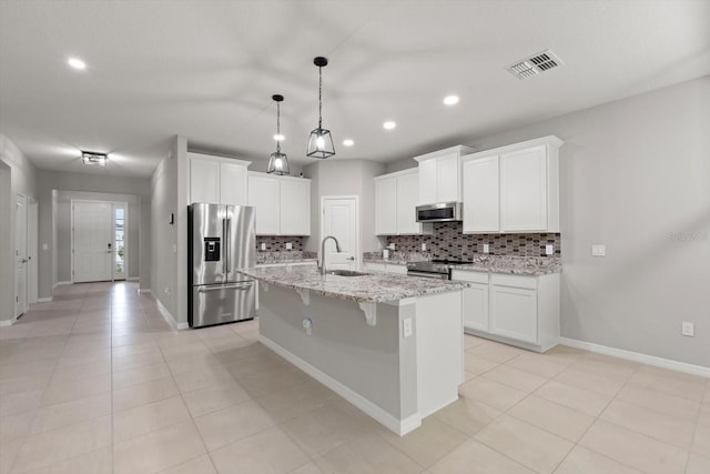 kitchen with a kitchen island with sink, stainless steel appliances, light stone counters, sink, and white cabinets