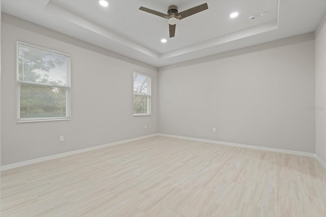 empty room featuring light hardwood / wood-style floors, ceiling fan, and a raised ceiling