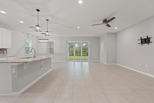 kitchen featuring white cabinets, decorative light fixtures, light stone counters, sink, and ceiling fan