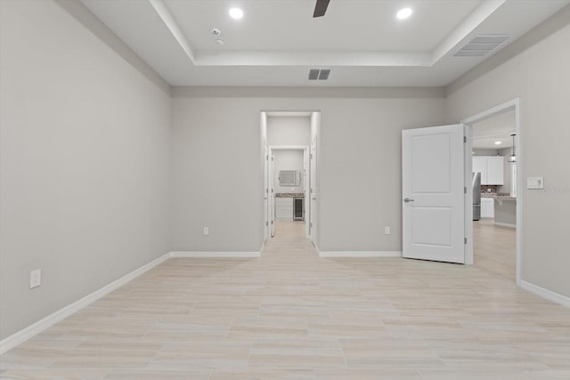 unfurnished bedroom with ceiling fan, a walk in closet, and a tray ceiling