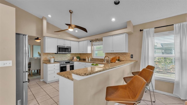 kitchen with white cabinetry, kitchen peninsula, appliances with stainless steel finishes, and vaulted ceiling