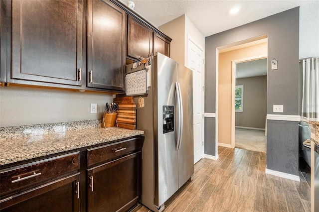 kitchen with a textured ceiling, dark brown cabinets, light stone counters, stainless steel refrigerator with ice dispenser, and light hardwood / wood-style floors