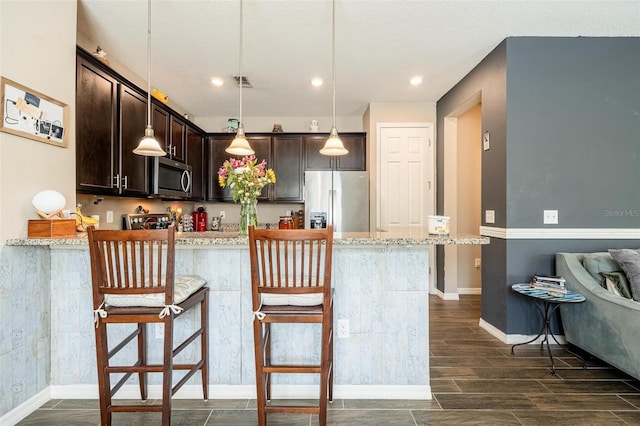 kitchen featuring a breakfast bar area, light stone counters, stainless steel appliances, and dark hardwood / wood-style floors