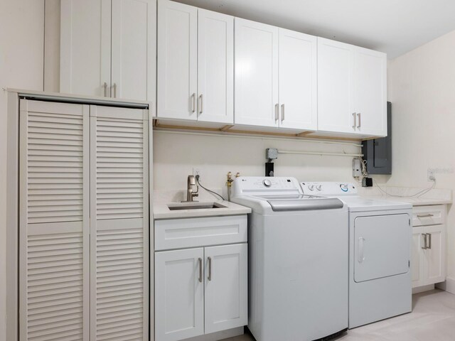 clothes washing area featuring electric panel, washing machine and clothes dryer, cabinets, and sink