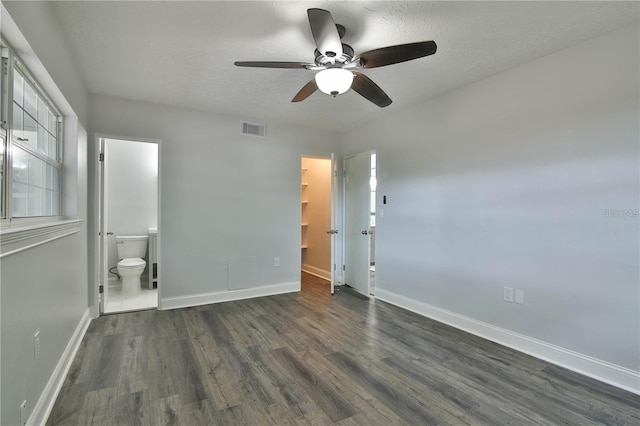 unfurnished bedroom with ceiling fan, a closet, dark wood-type flooring, a spacious closet, and ensuite bathroom