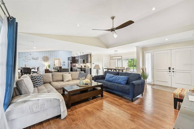 living room with ceiling fan, light hardwood / wood-style floors, and vaulted ceiling