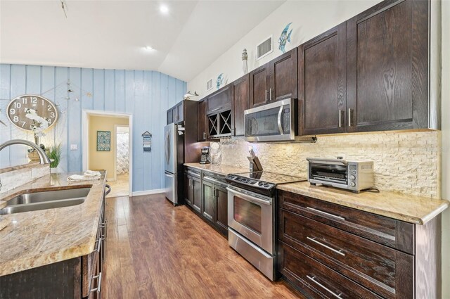 kitchen with dark wood finished floors, a sink, stainless steel appliances, dark brown cabinets, and tasteful backsplash