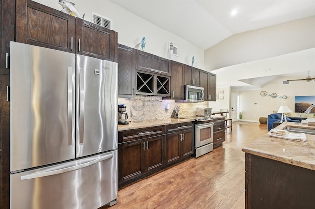 kitchen featuring backsplash, open floor plan, lofted ceiling, light wood-style flooring, and stainless steel appliances