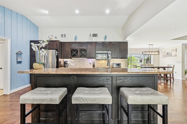 kitchen featuring a kitchen breakfast bar, dark hardwood / wood-style flooring, a kitchen island with sink, stainless steel appliances, and lofted ceiling