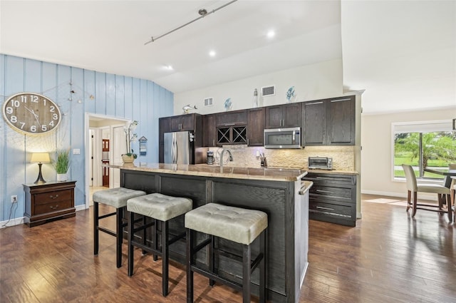 kitchen with a kitchen island with sink, vaulted ceiling, stainless steel appliances, and dark hardwood / wood-style floors