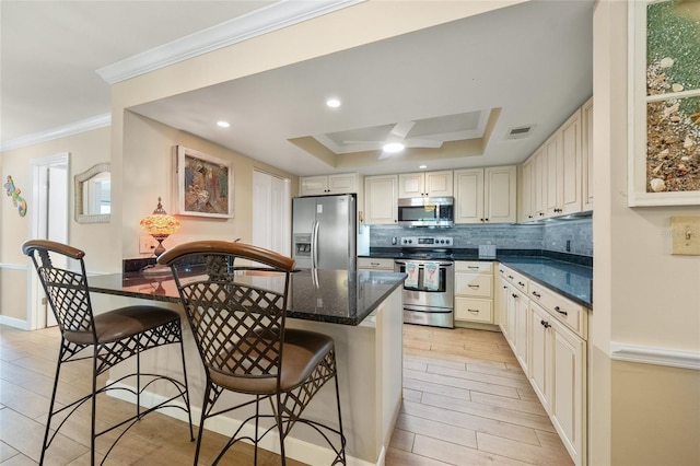 kitchen with appliances with stainless steel finishes, backsplash, ornamental molding, a breakfast bar, and a raised ceiling