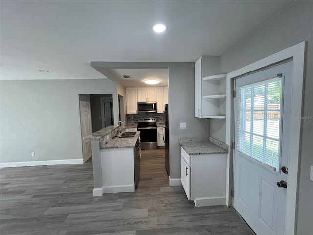 kitchen featuring light stone countertops, hardwood / wood-style floors, appliances with stainless steel finishes, kitchen peninsula, and white cabinets