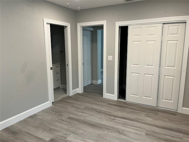 unfurnished bedroom featuring light hardwood / wood-style flooring, ensuite bathroom, and a closet