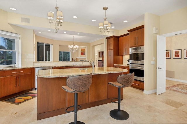 kitchen featuring appliances with stainless steel finishes, a breakfast bar, an inviting chandelier, decorative light fixtures, and a center island with sink