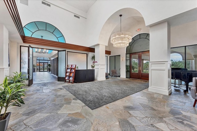 foyer featuring a notable chandelier, decorative columns, and high vaulted ceiling