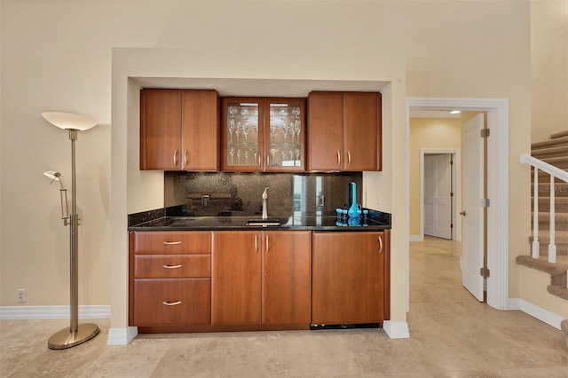 kitchen featuring glass insert cabinets, brown cabinets, backsplash, and baseboards