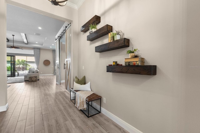 hall with a barn door, crown molding, and light hardwood / wood-style flooring