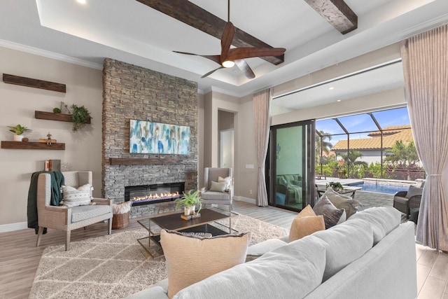 living room with beamed ceiling, a stone fireplace, light hardwood / wood-style flooring, and crown molding