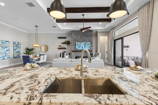 kitchen with a fireplace, beam ceiling, sink, and light stone counters