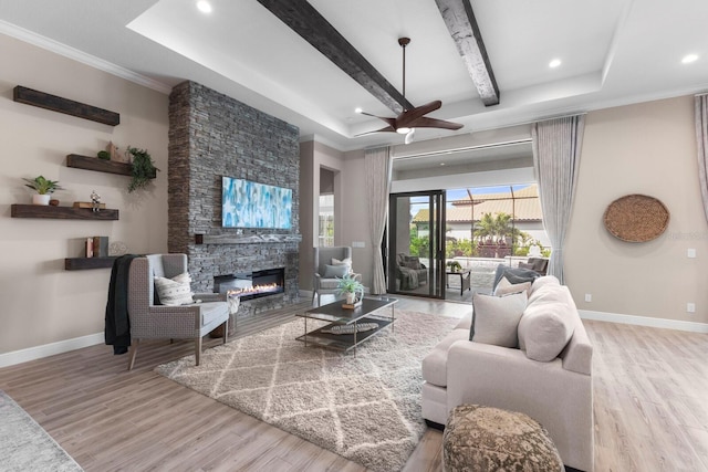 living room with beamed ceiling, ornamental molding, ceiling fan, a stone fireplace, and light wood-type flooring