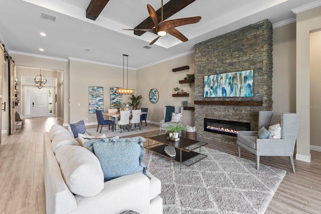 living room with a stone fireplace, light wood-type flooring, ceiling fan with notable chandelier, and ornamental molding