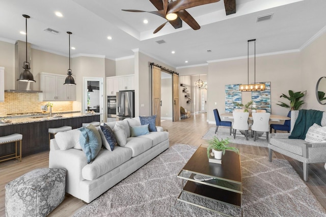 living room with ceiling fan with notable chandelier, a barn door, hardwood / wood-style flooring, sink, and ornamental molding