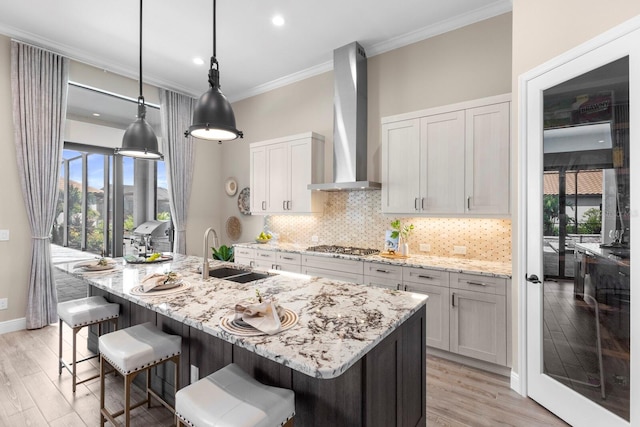 kitchen with white cabinetry, sink, light stone countertops, wall chimney range hood, and pendant lighting