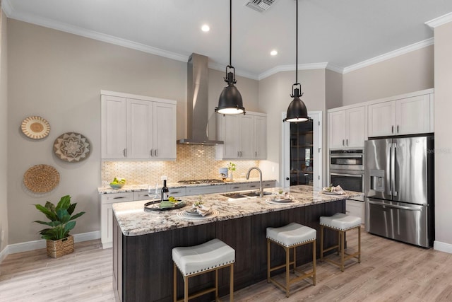 kitchen featuring sink, appliances with stainless steel finishes, wall chimney exhaust hood, an island with sink, and white cabinets