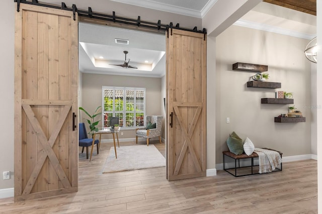 entryway with crown molding, a barn door, a raised ceiling, hardwood / wood-style floors, and ceiling fan