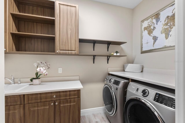 clothes washing area with separate washer and dryer, cabinets, light wood-type flooring, and sink