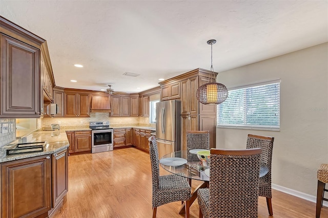 kitchen featuring hanging light fixtures, tasteful backsplash, light hardwood / wood-style floors, light stone counters, and stainless steel appliances