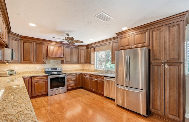 kitchen featuring appliances with stainless steel finishes, light stone counters, custom range hood, sink, and light hardwood / wood-style flooring