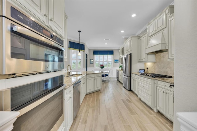 kitchen featuring sink, light stone countertops, hanging light fixtures, appliances with stainless steel finishes, and light hardwood / wood-style floors