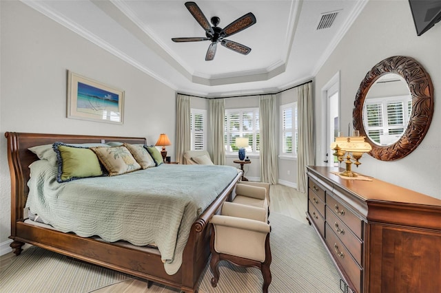 bedroom with light hardwood / wood-style flooring, ceiling fan, ornamental molding, and a tray ceiling