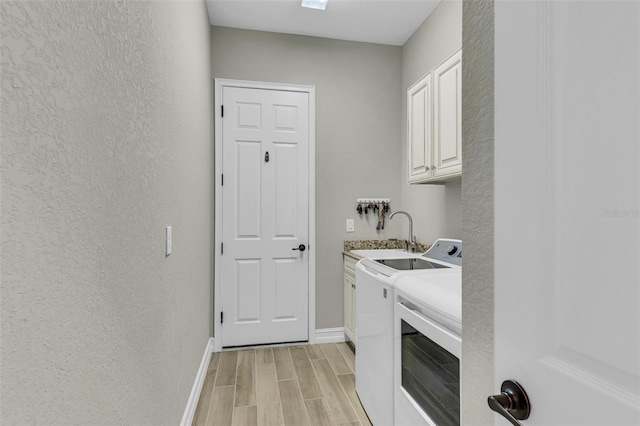 laundry room featuring light hardwood / wood-style flooring, washing machine and dryer, cabinets, and sink