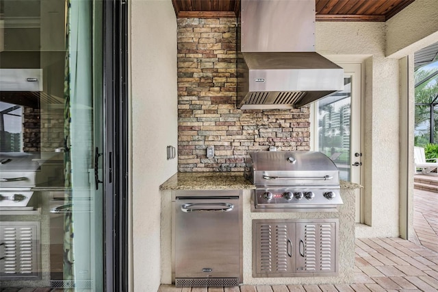 kitchen featuring crown molding, stainless steel fridge, light stone countertops, and wall chimney exhaust hood