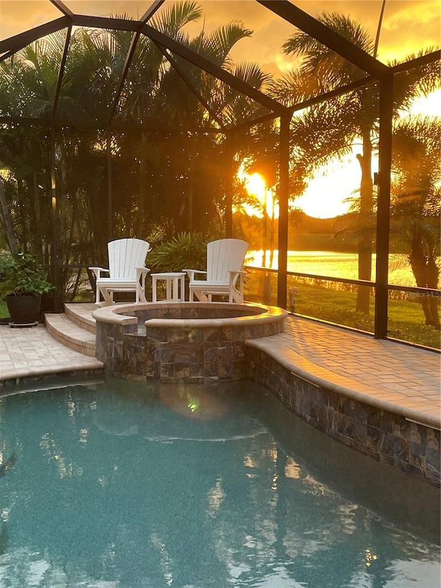 pool at dusk featuring a water view, a lanai, and a patio