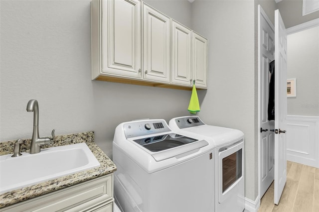 clothes washing area with washer and dryer, cabinets, sink, and light hardwood / wood-style floors