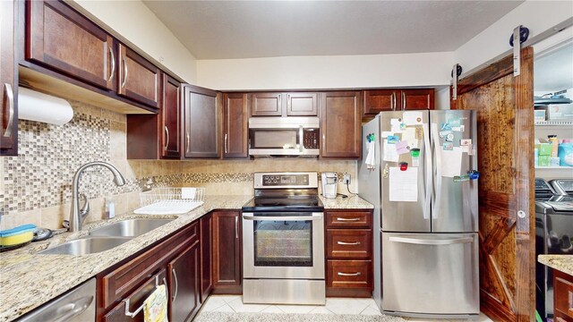 kitchen with sink, a barn door, stainless steel appliances, independent washer and dryer, and light tile patterned floors