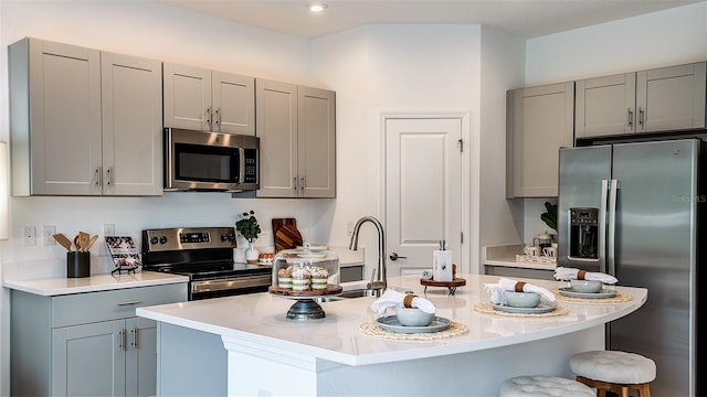 kitchen featuring a kitchen island with sink, appliances with stainless steel finishes, gray cabinets, and a breakfast bar